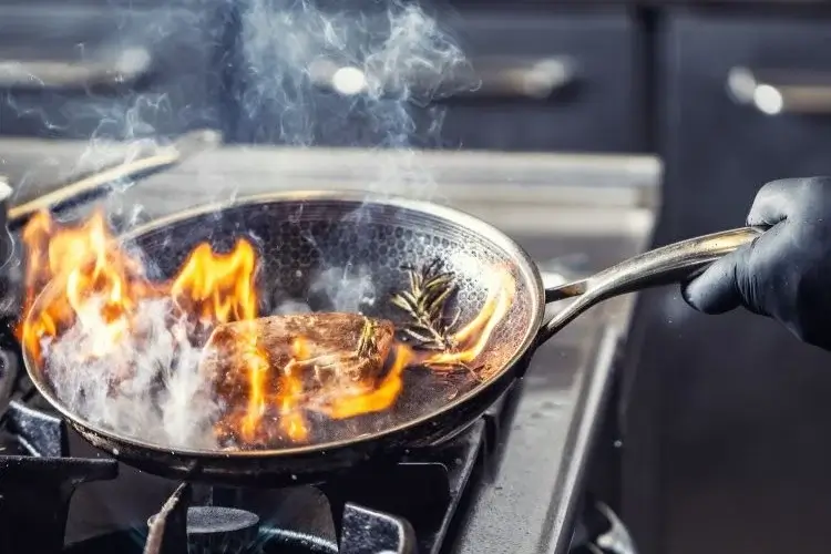 une main tien une poêle avec des aliment qui brule sans respecter les aliment et le cuisson basse température